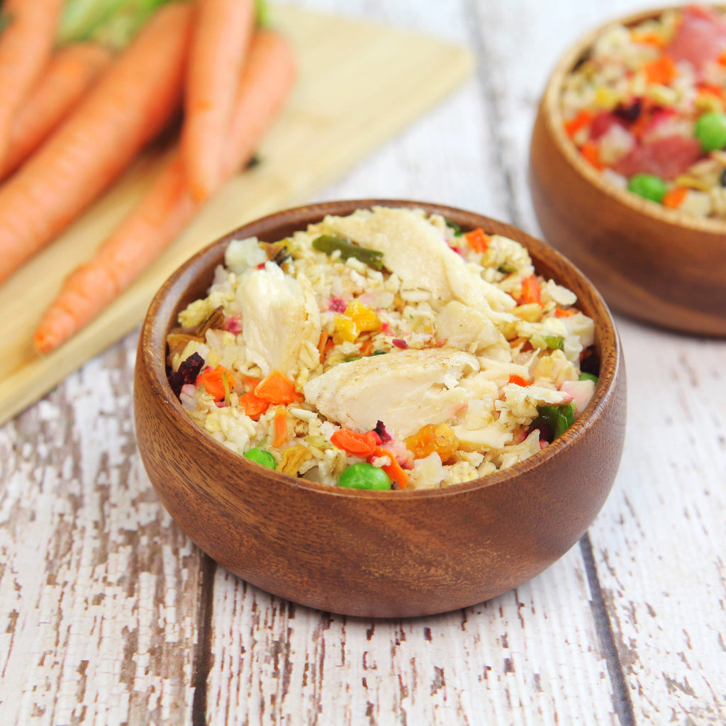 Two wooden bowls of chicken and vegetable rice with diced carrots, peas, and peppers; fresh carrots in background.