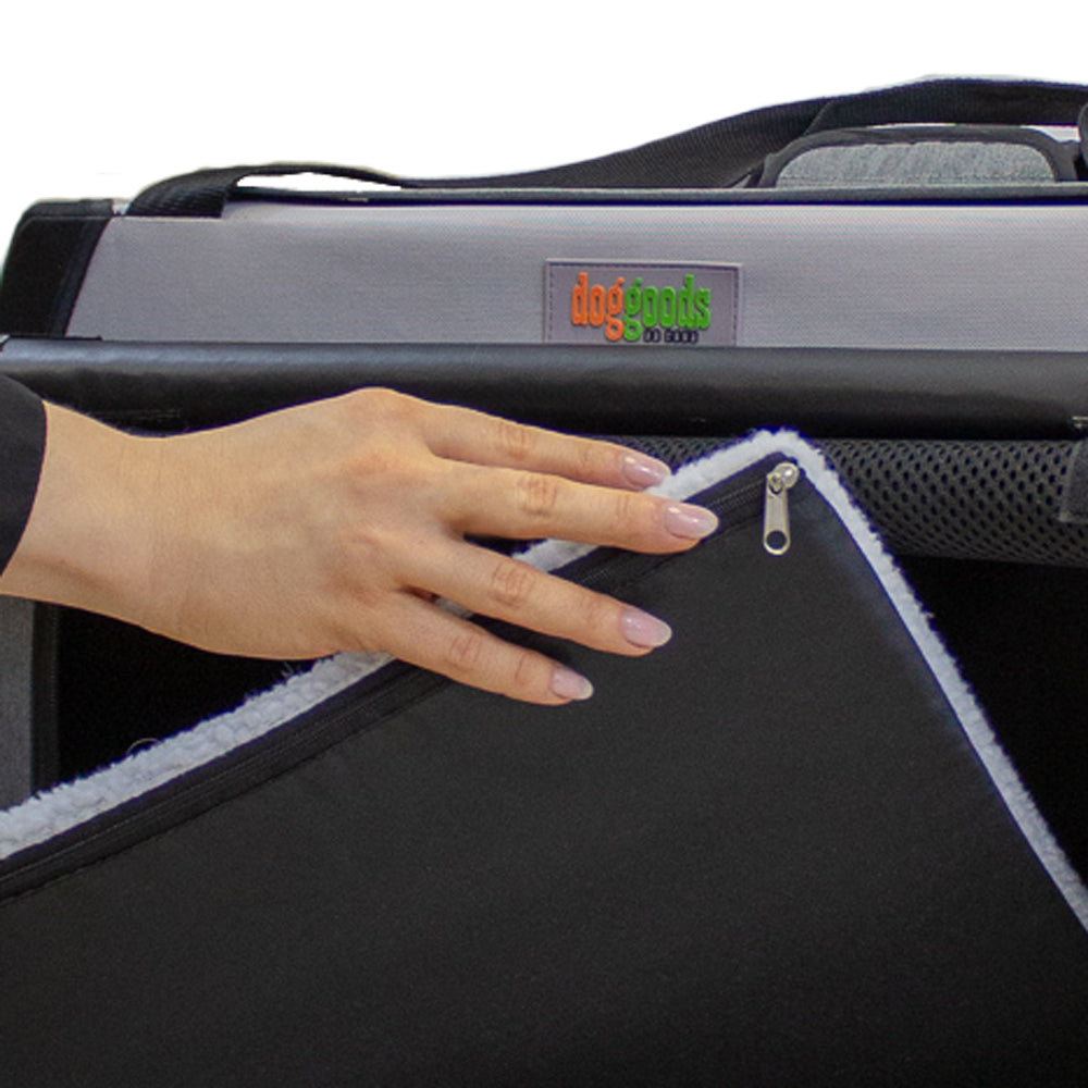 Close-up of a hand adjusting the soft fleece mat inside a DogGoods foldable crate. The mat is zippered, liquid-resistant, and fully washable for pet comfort.