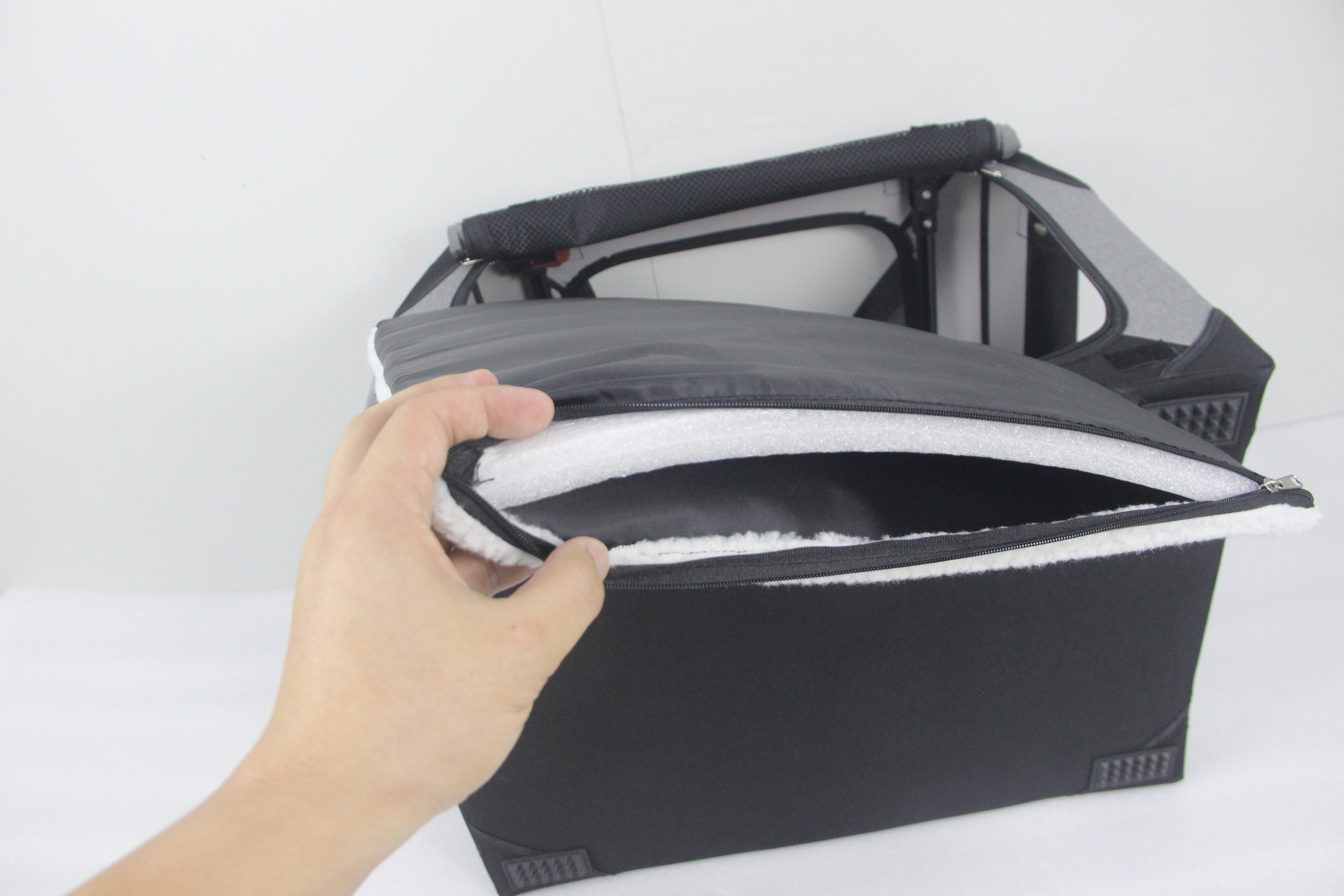 Close-up of a hand opening the zippered soft fleece mat of a DogGoods foldable crate. The mat is padded, liquid-resistant, and fully washable for pet comfort.