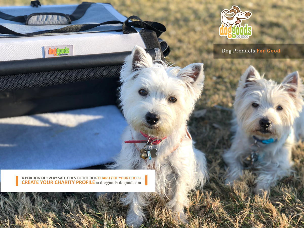 Two white terrier dogs standing on grass in front of a DogGoods foldable travel crate. The crate is open, showing a soft fleece mat inside. A banner at the bottom highlights that a portion of every sale goes to a dog charity of the customer's choice. The DogGoods logo and tagline, "Dog Products For Good," are displayed in the top right corner.