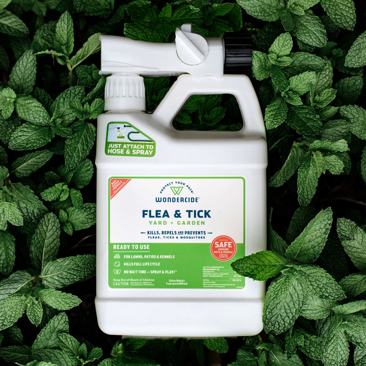 A white bottle of Wondercide Ready-to-Use Flea & Tick Spray for Yard + Garden sits on green mint leaves, featuring a hose attachment and green label that highlights its pet- and family-safe formula for flea and tick protection.