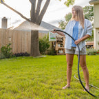 A woman in a light blue shirt and khaki shorts stands barefoot on grass, using Wondercide Ready-to-Use Flea & Tick Spray for Yard + Garden to protect her backyard from pests on a sunny day.
