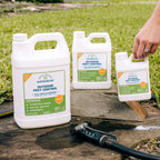 Three Wondercide Outdoor Pest Control Concentrate for Yard + Garden containers are on a wooden plank outside with grass in the background. A hand holds the smallest, and a garden hose nozzle—perfect for applying this mosquito repellent—is nearby.