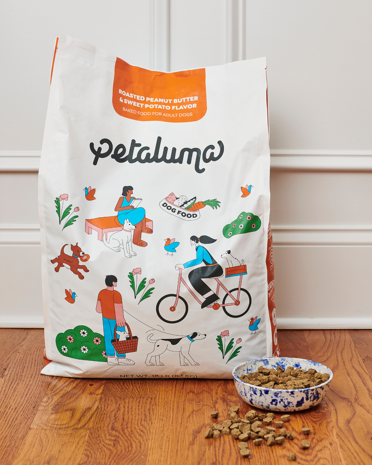Petaluma dog food bag with a bowl of dog food on a wooden floor