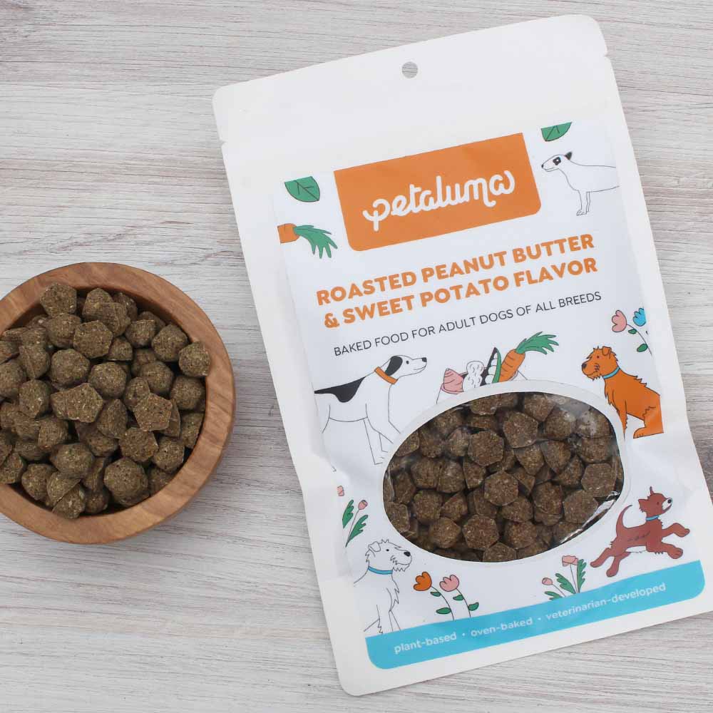 Petaluma adult dog food sample pouch next to a wooden bowl of baked food