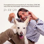 A man in a plaid shirt sits with a white dog, playfully lifting its ears. Text above highlights Dr. Rob Silver’s support for cognitive health in pets using Real Mushrooms’ Lion's Mane with Qrill™ Pet – 12 Units.