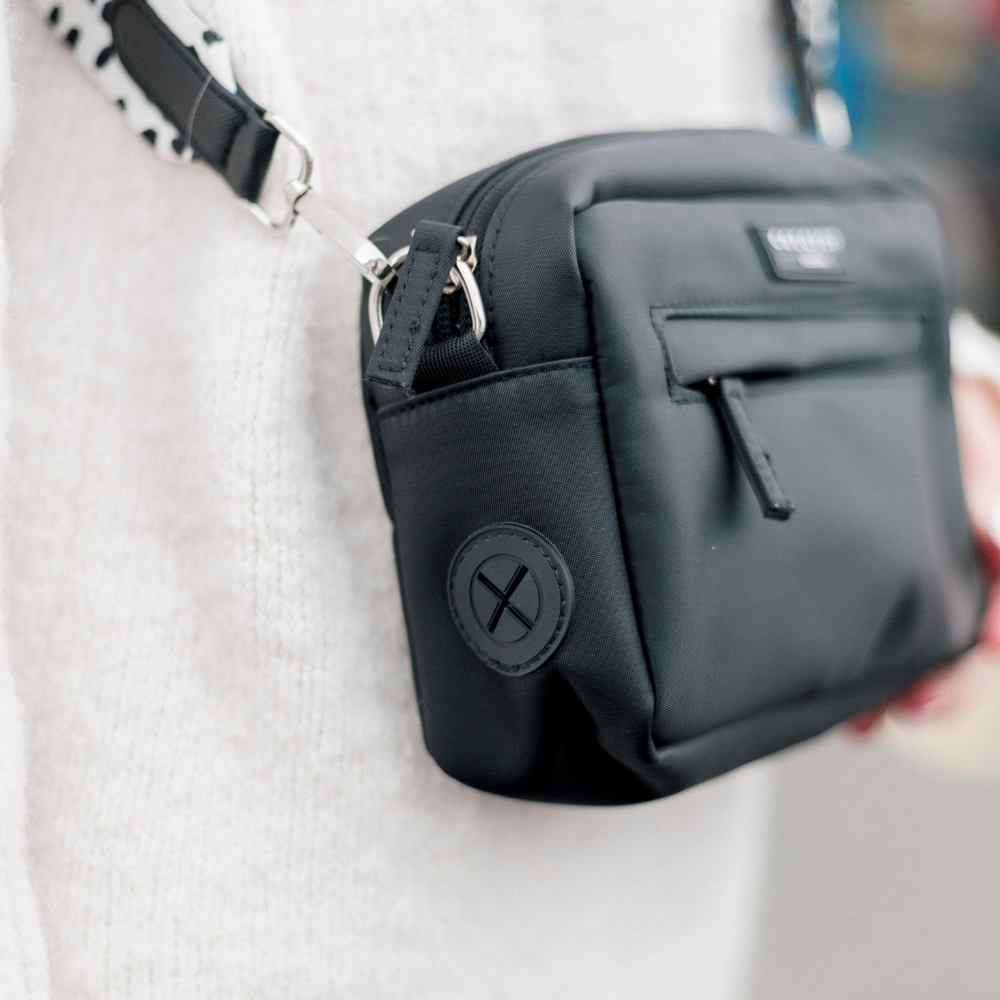 Black Cocopup London dog walking bag worn crossbody over a white sweater.