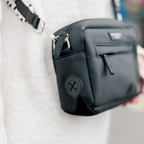 Black Cocopup London dog walking bag worn crossbody over a white sweater.