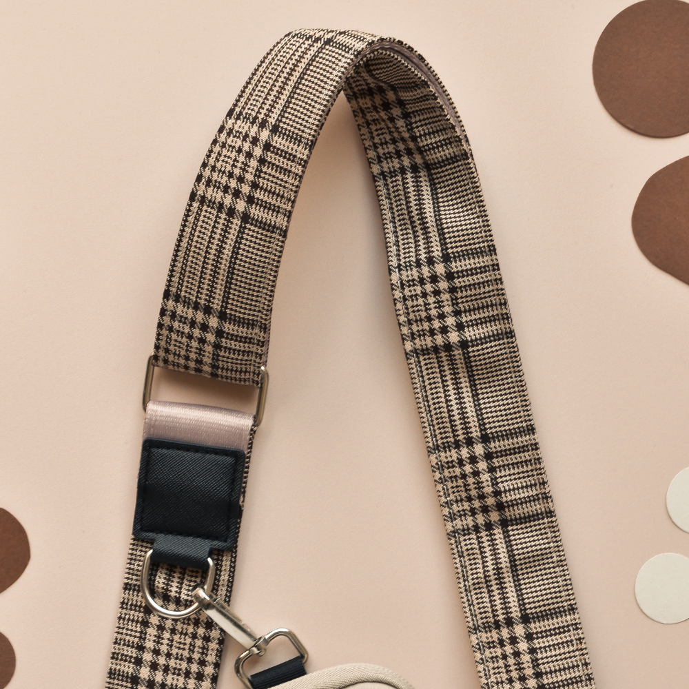 Black plaid Cocopup London dog walking bag strap with metal clasps, displayed on overlapping paper circles.