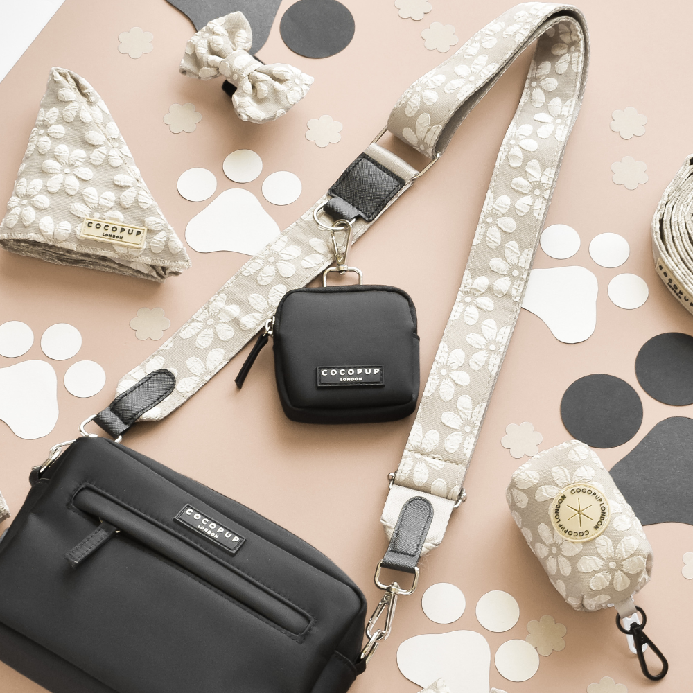 Black dog walking bag with matching leash, bow, and poop bag dispenser arranged flat on a light surface.