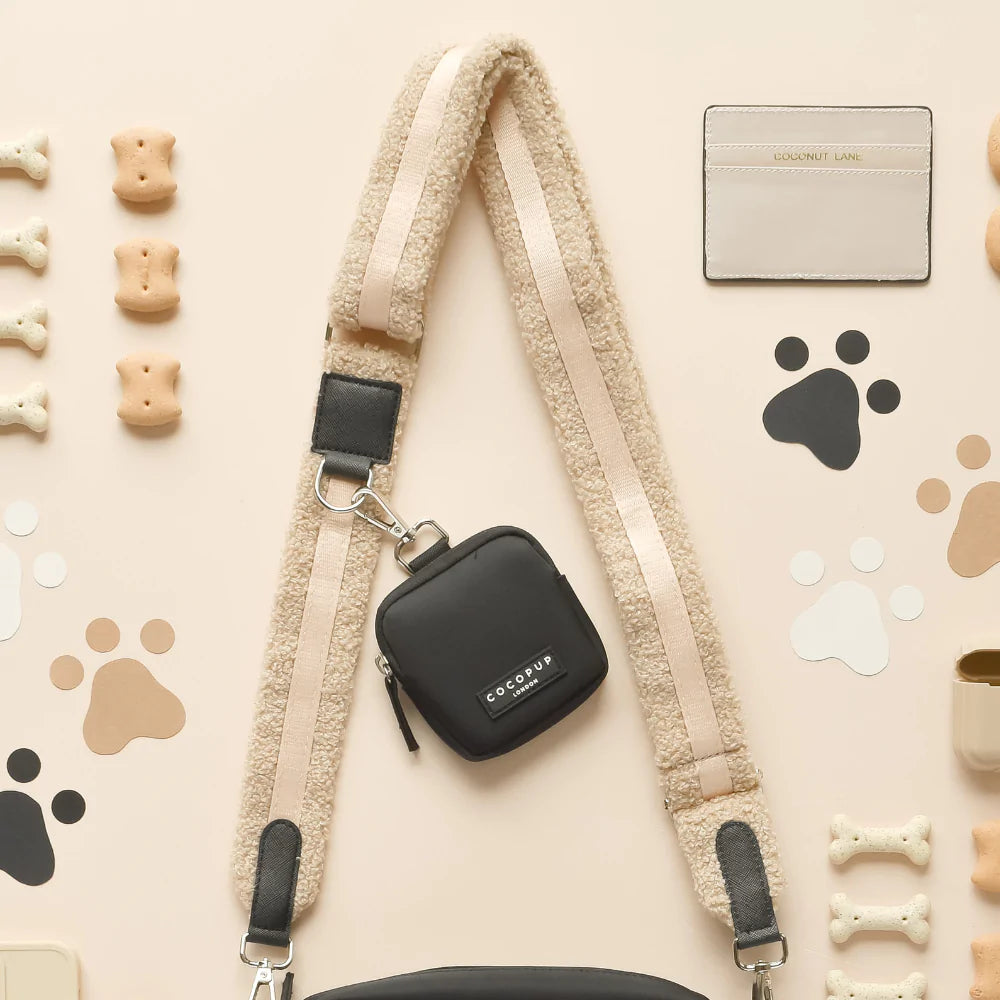Black Cocopup London dog walking bag, dog treats, cream card holder, and paw prints on a beige background.