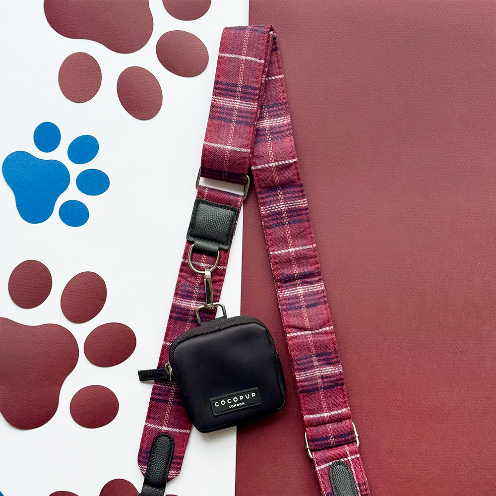 Black Cocopup London dog walking bag with maroon plaid leash on a paw print background.