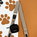 Black Cocopup London dog walking bag with a plaid leash, displayed on a paw print background.