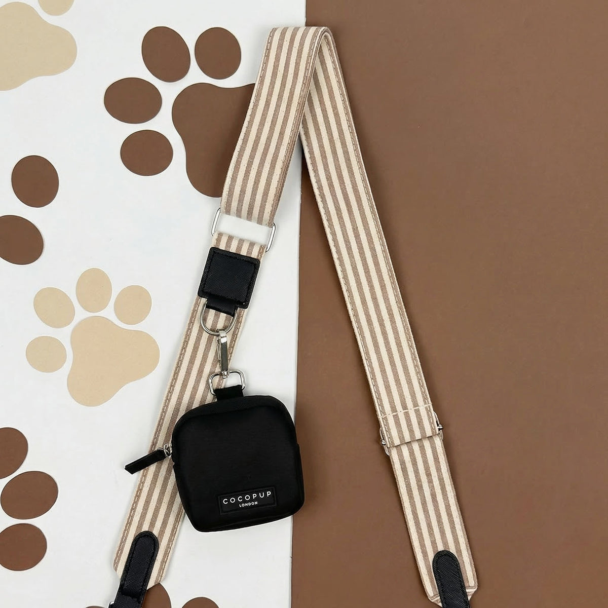 Black Cocopup London dog walking bag with attachable treat pouch, displayed on a paw print patterned background.
