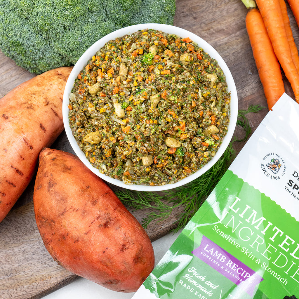 Dr. Pol's Limited Ingredient Lamb Recipe pet food bag beside a bowl of fresh food, sweet potatoes, broccoli, and carrots