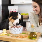 Woman smiling as a tricolor Border Collie eats from a bowl of raw dog food on a wooden cutting board