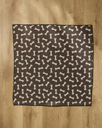 The Geometry Sweet Treats mat is a brown, square dog mat featuring a white bone pattern, made from absorbent towel material, and placed on a wooden floor.