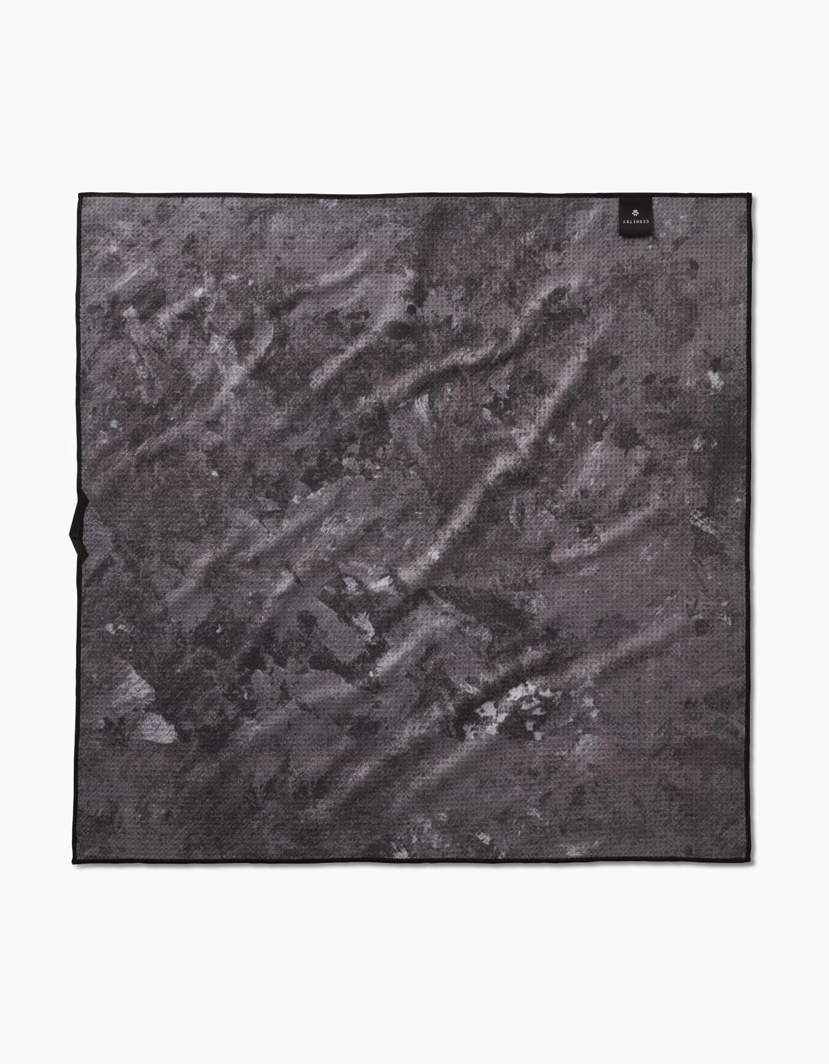 The Geometry Sweet Treats is a square microfiber dog towel in black and gray with a subtle abstract design and a small black label in one corner. Made from absorbent recycled materials, the towel is shown flat on a white background.