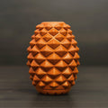The Conifur: a terracotta-colored ceramic vase with a geometric diamond-textured surface—evoking the look of a dog enrichment toy—set against a dark, blurred background.