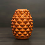 The Conifur: a terracotta-colored ceramic vase with a geometric diamond-textured surface—evoking the look of a dog enrichment toy—set against a dark, blurred background.