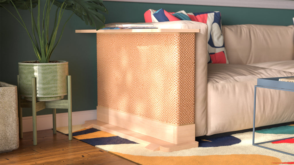 A Cat-e-Corner table placed next to a sofa, integrating a cat's scratching post with a small table, in a room with a plant and a colorful cushion.
