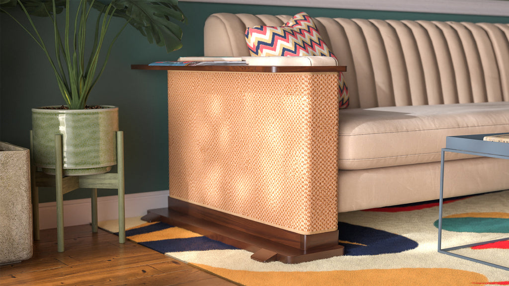 A Cat-e-Corner table placed next to a sofa, integrating a cat's scratching post with a small table, in a room with a plant and a colorful cushion.