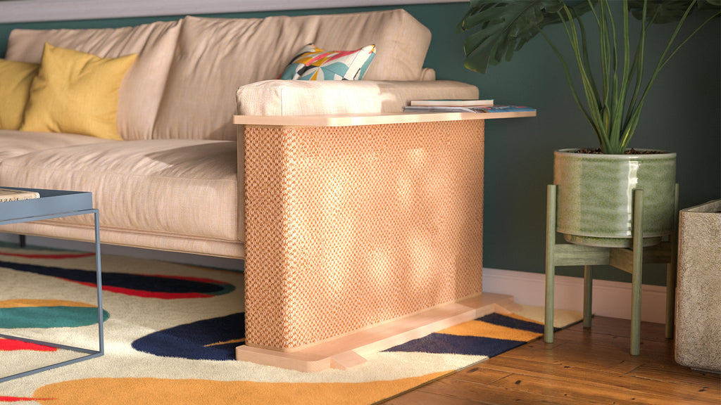 A Cat-e-Corner table placed next to a sofa, integrating a cat's scratching post with a small table, in a room with a plant and a colorful cushion.