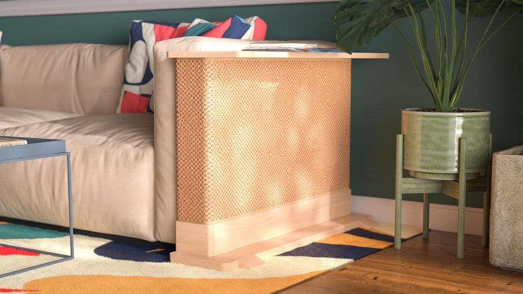 A Cat-e-Corner table placed next to a sofa, integrating a cat's scratching post with a small table, in a room with a plant and a colorful cushion.