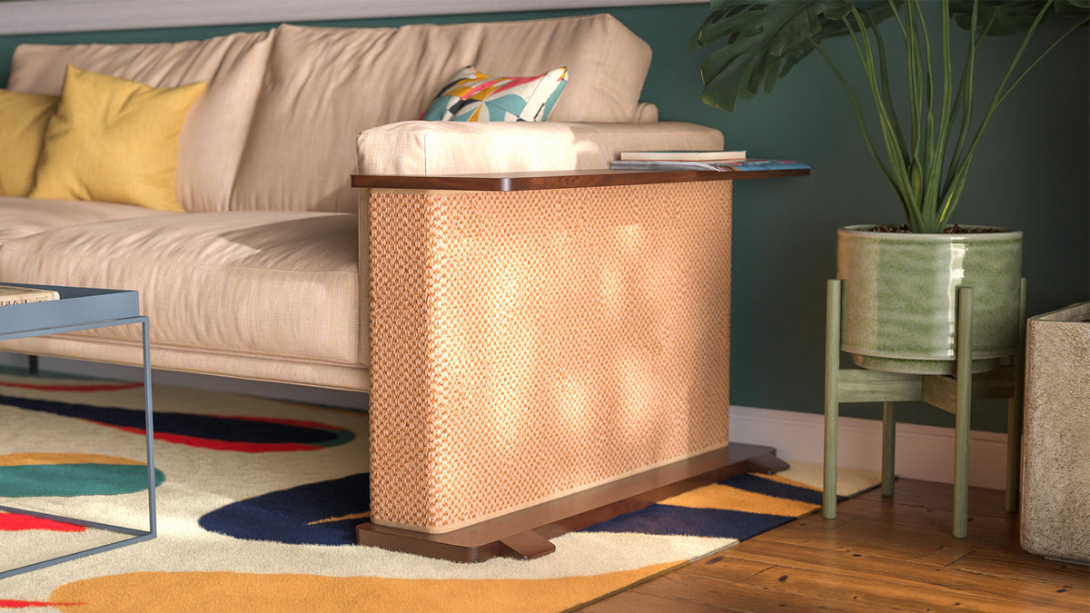 A Cat-e-Corner table placed next to a sofa, integrating a cat's scratching post with a small table, in a room with a plant and a colorful cushion.