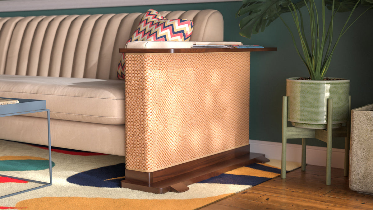 A Cat-e-Corner table placed next to a sofa, integrating a cat's scratching post with a small table, in a room with a plant and a colorful cushion.