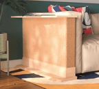 A Cat-e-Corner table placed next to a sofa, integrating a cat's scratching post with a small table, in a room with a plant and a colorful cushion.