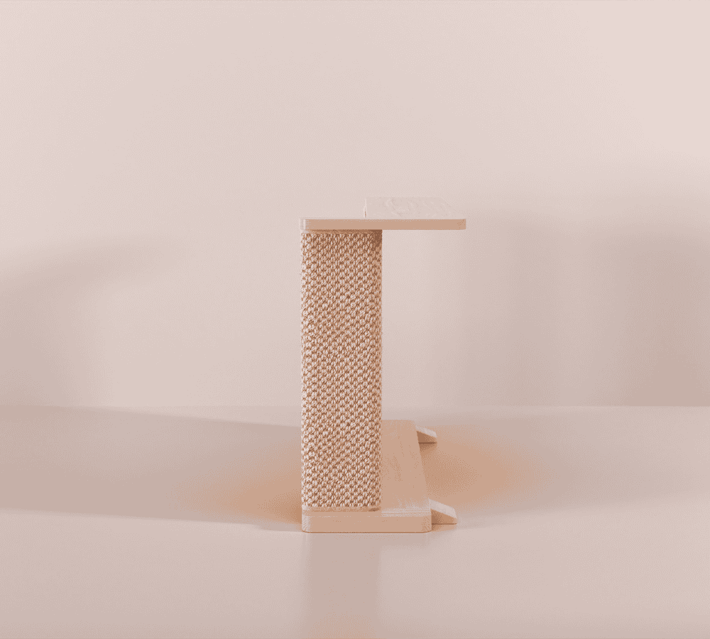 A Cat-e-Corner table placed next to a sofa, integrating a cat's scratching post with a small table, in a room with a plant and a colorful cushion.