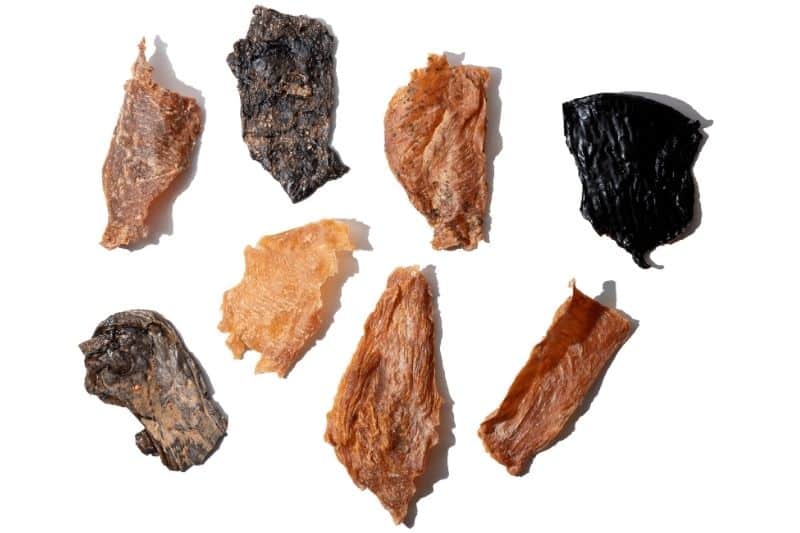 Top-down view of Uncle Justy’s Just Chicken jerky pieces showcasing dehydrated chicken strips on white background