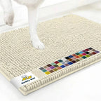 Angled view of Muddy Mat® anti-mud dog door mat in ivory showing plush chenille texture, color swatches, and dog paw on a white floor