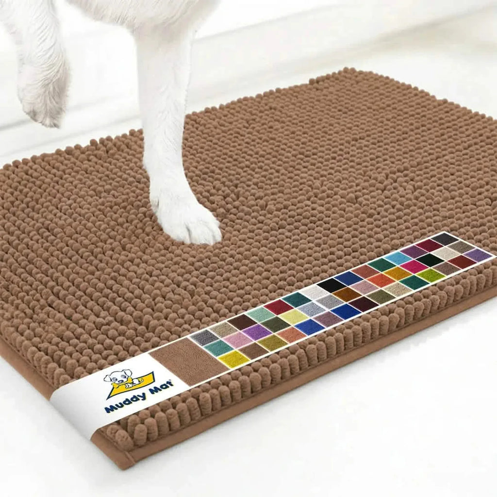 Close-up of Muddy Mat anti-mud dog door mat in mocha showing chenille nub texture, color swatch strip, and a dog paw on a white floor