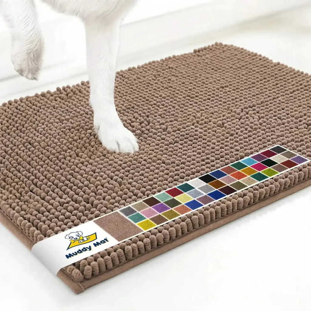 Angled view of Muddy Mat anti-mud dog door mat in tan showing textured chenille nubs, color swatch strip, and a dog paw on a white floor