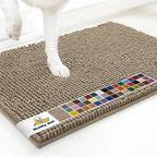 Close up of Muddy Mat anti mud dog door mat in taupe showing textured chenille surface, color swatch band and a dog’s paw on a white floor