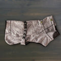 A Fleece Jacket for dogs in gray and black, featuring textured fabric, green cord locks, and an adjustable strap, is shown laid flat on a dark wooden surface.