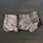 A Fleece Jacket for dogs in gray and black, featuring textured fabric, green cord locks, and an adjustable strap, is shown laid flat on a dark wooden surface.